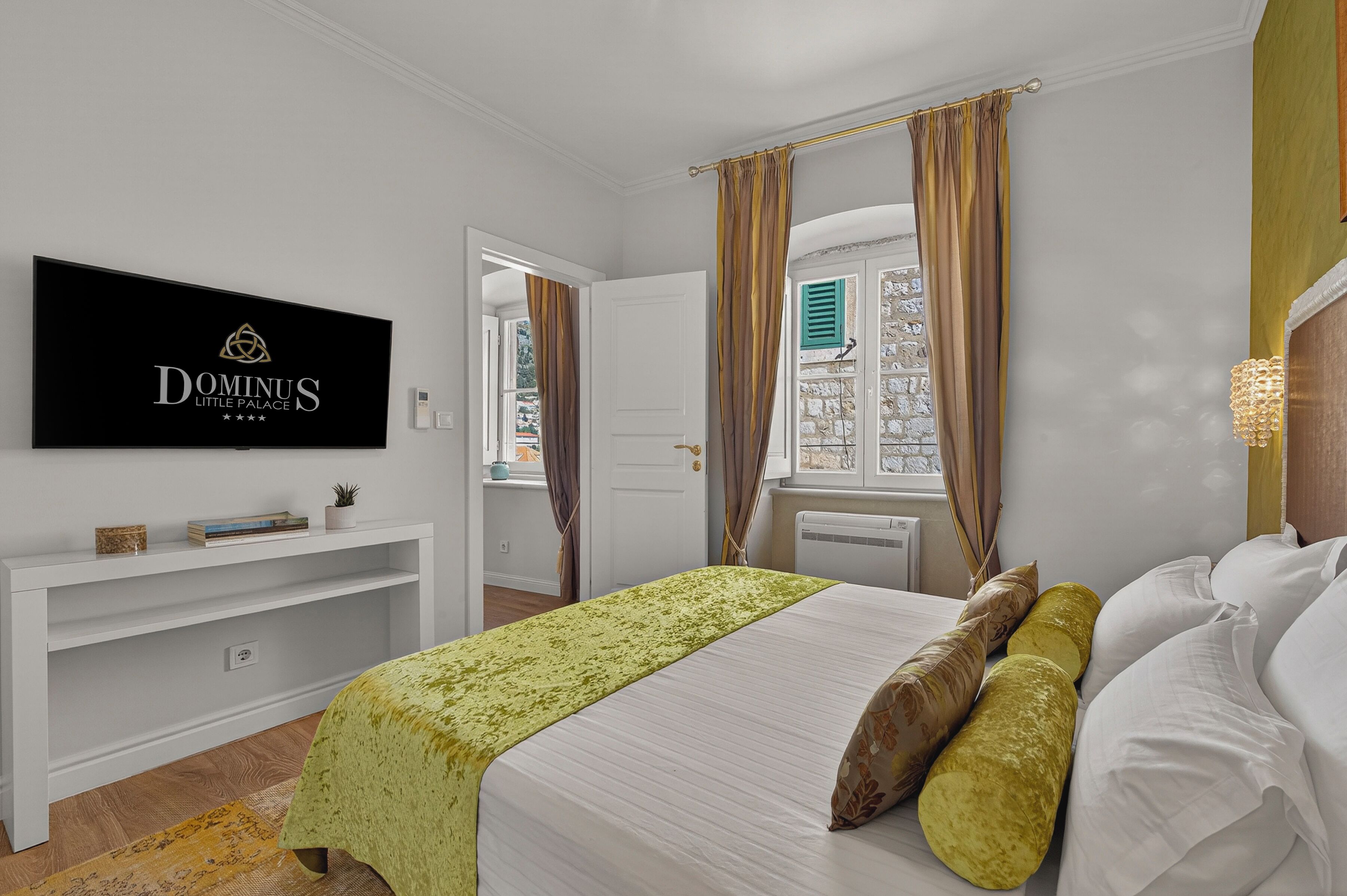 Hotelkamer met een bed, een televisie aan de muur, een raam met gordijnen en een klein plankje met spullen.