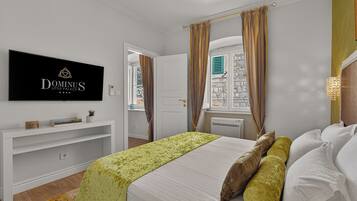 Hotelkamer met een bed, een televisie aan de muur, een raam met gordijnen en een klein plankje met spullen.