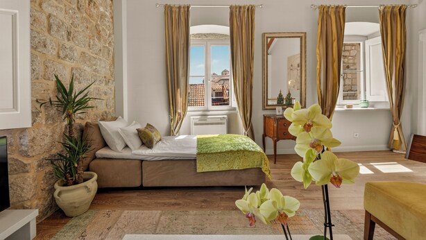 Una habitación con pared de piedra, una cama, un escritorio y una ventana con cortinas.