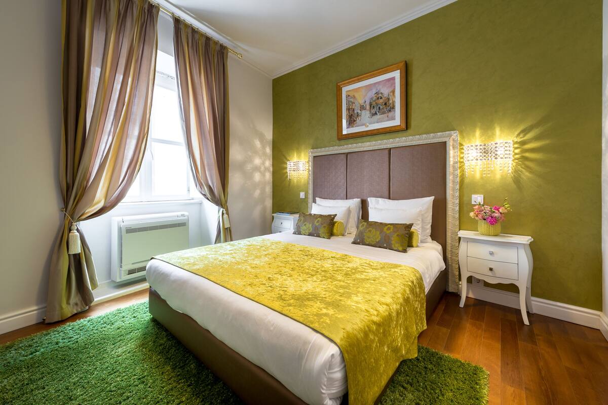 Ein Schlafzimmer mit einem Bett, grünen Wänden, einem Bild an der Wand und einem Nachttisch mit einer Lampe.