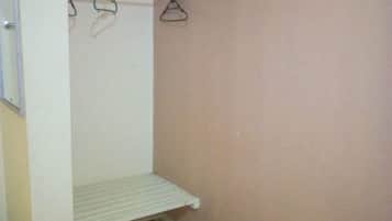 Une petite pièce avec une table en bois, une étagère blanche et un portant à vêtements avec des cintres.