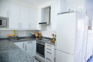 A modern kitchen with white cabinetry, a granite countertop, stainless steel appliances, and a built-in oven.