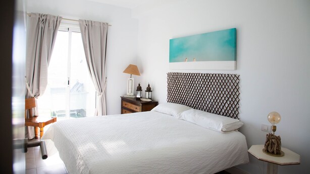 A neatly arranged bedroom with a bed, a nightstand, a lamp, and a painting on the wall. - At sea level, and overlooking the beach.  Apartment with terrace and 8 hrs of sun (Porís de Abona)