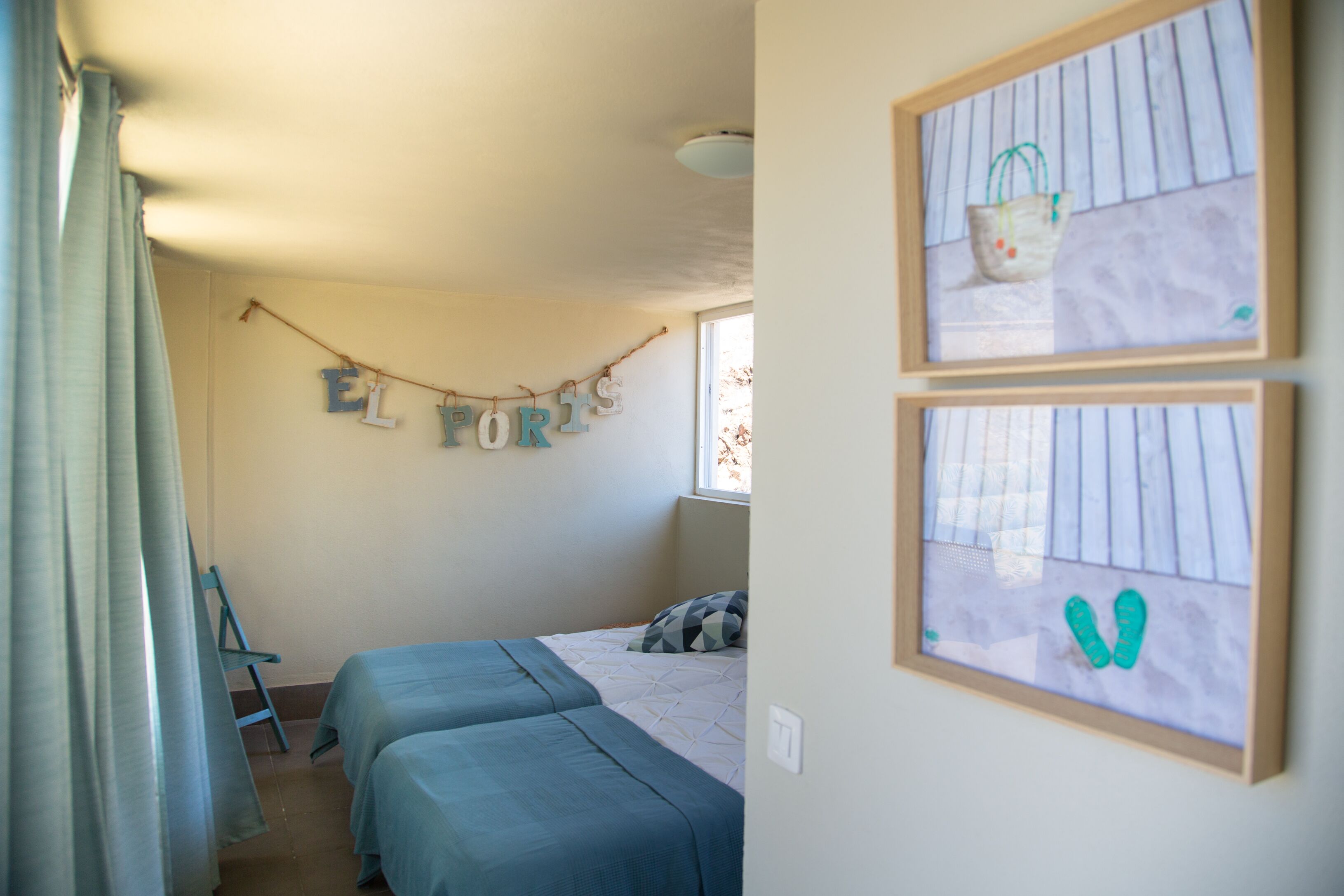 Een slaapkamer met twee bedden, een lichtletterslinger aan de muur en een lijst met een afbeelding.