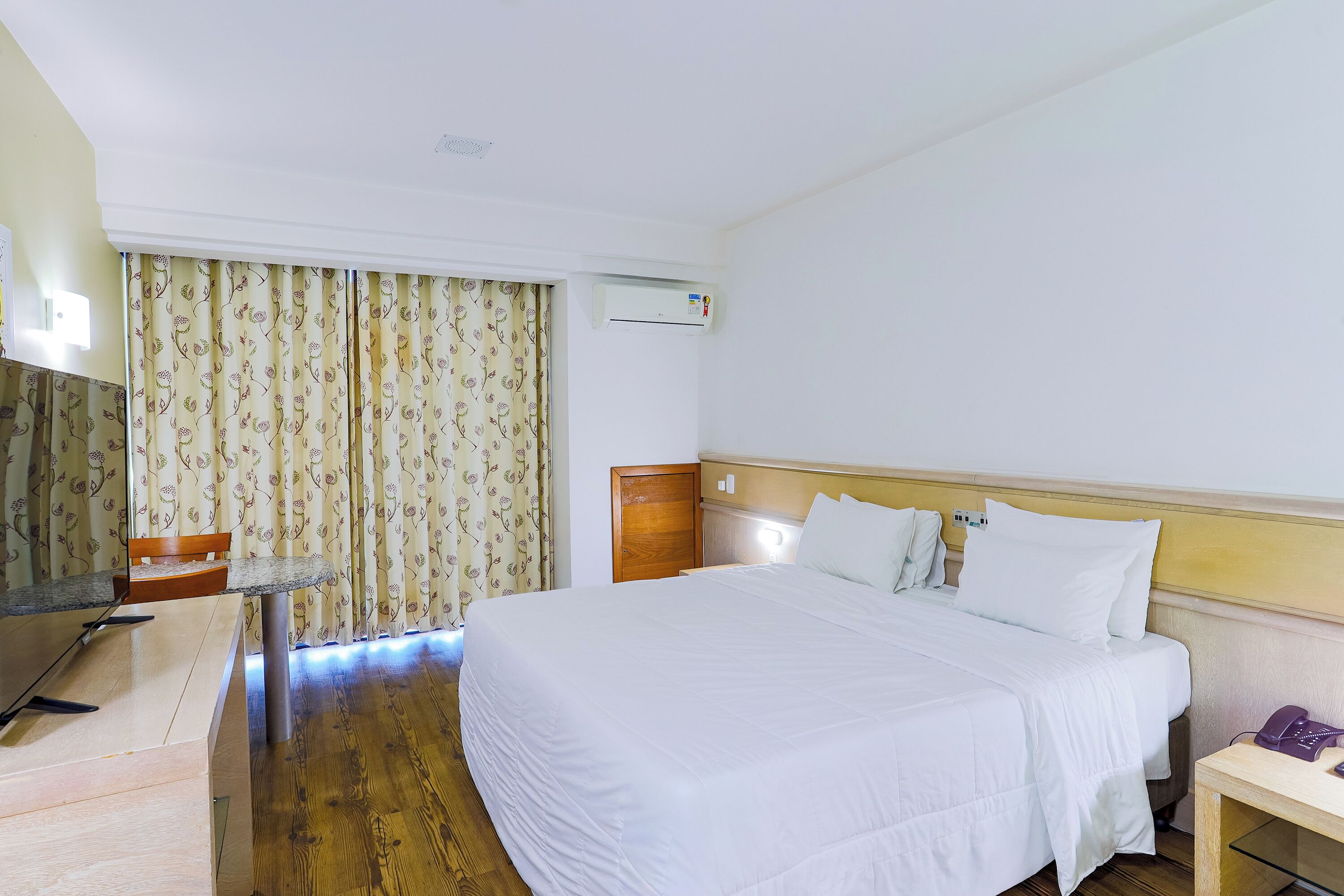 Habitación de hotel con cama, escritorio, silla, teléfono y aire acondicionado.