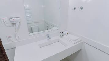 Un baño moderno con lavamanos blanco, espejo, secador de pelo y artículos de aseo.
