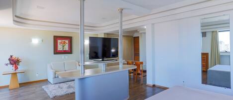 A modern hotel room with a large bed, a TV, a dining area, and a bathroom visible through an open door.