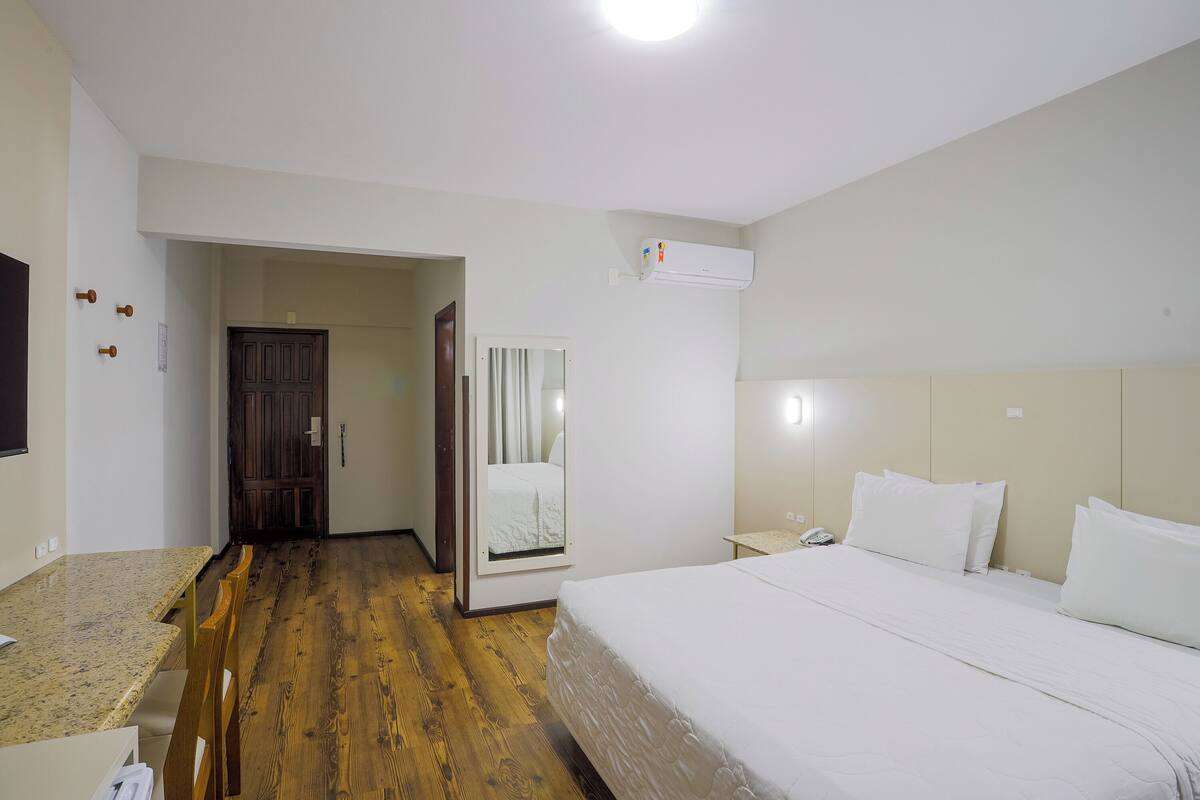 Hotellihuone, jossa on sänky, työpöytä, tuoli, puulattia, ovi ja ilmastointilaite.