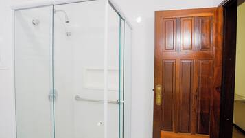 Ducha con cerramiento de vidrio y puerta de madera contigua.