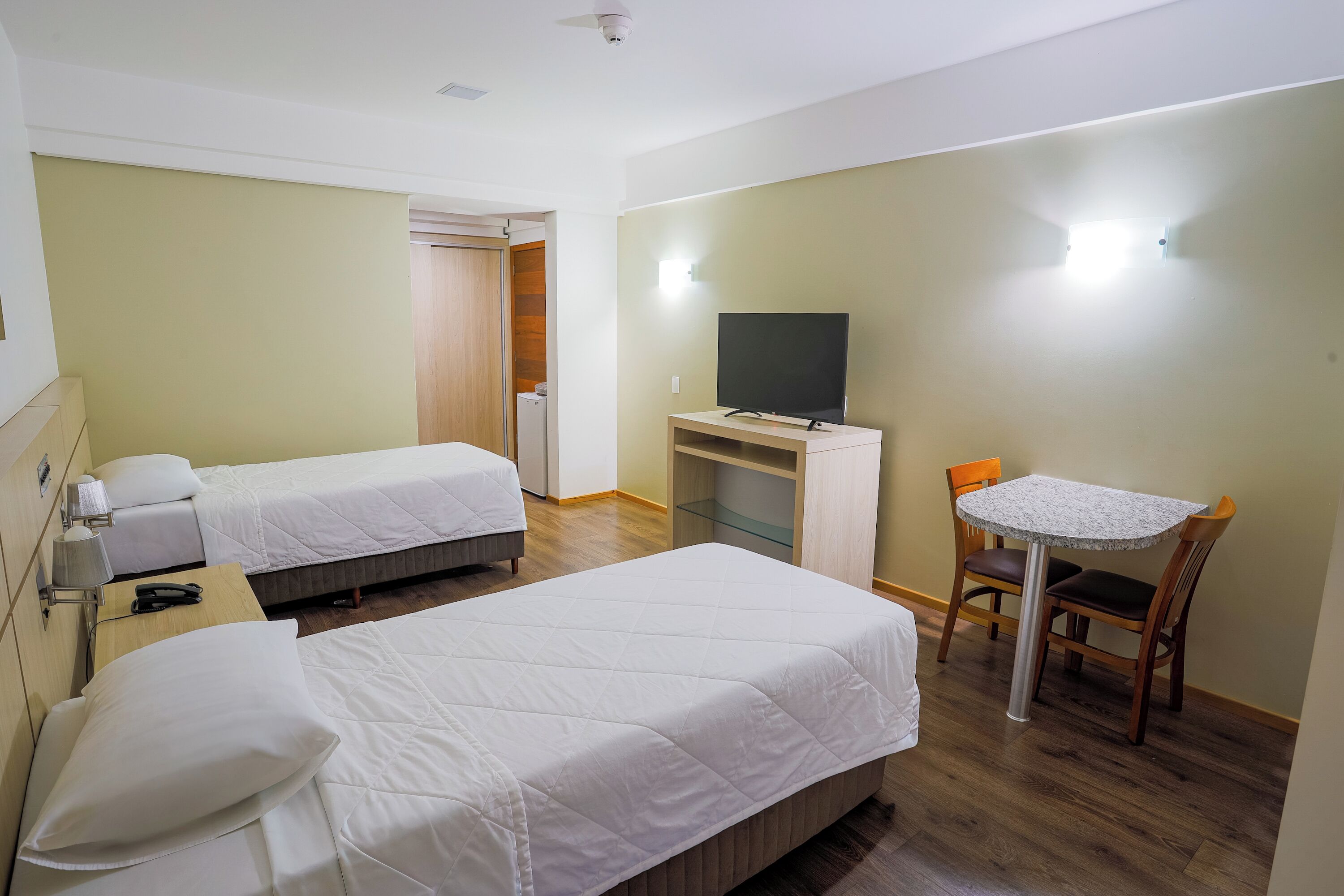 A hotel room with two single beds, a desk with a television, and a small table with chairs.