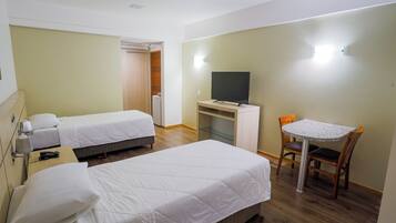 A hotel room with two single beds, a desk with a television, and a small table with chairs.