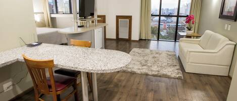 Habitación de hotel moderna con comedor, sofá, televisión y vista a la ciudad.
