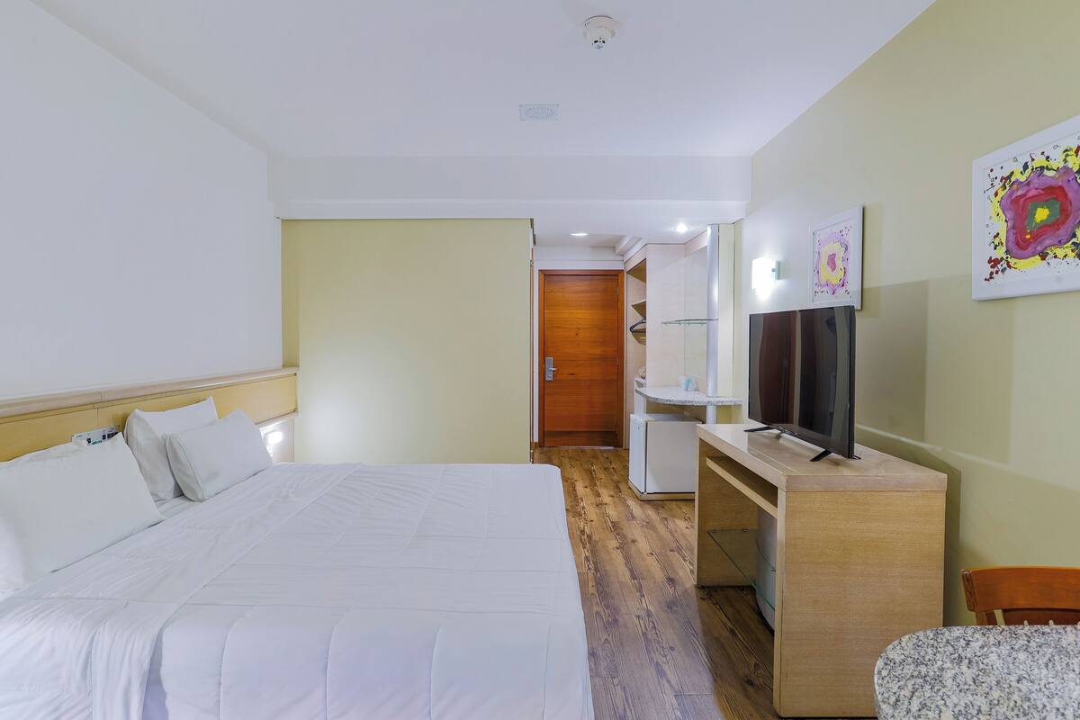 Hotellihuone, jossa on sänky, työpöytä, jossa on televisio, tuoli ja ovi, joka johtaa kylpyhuoneeseen.