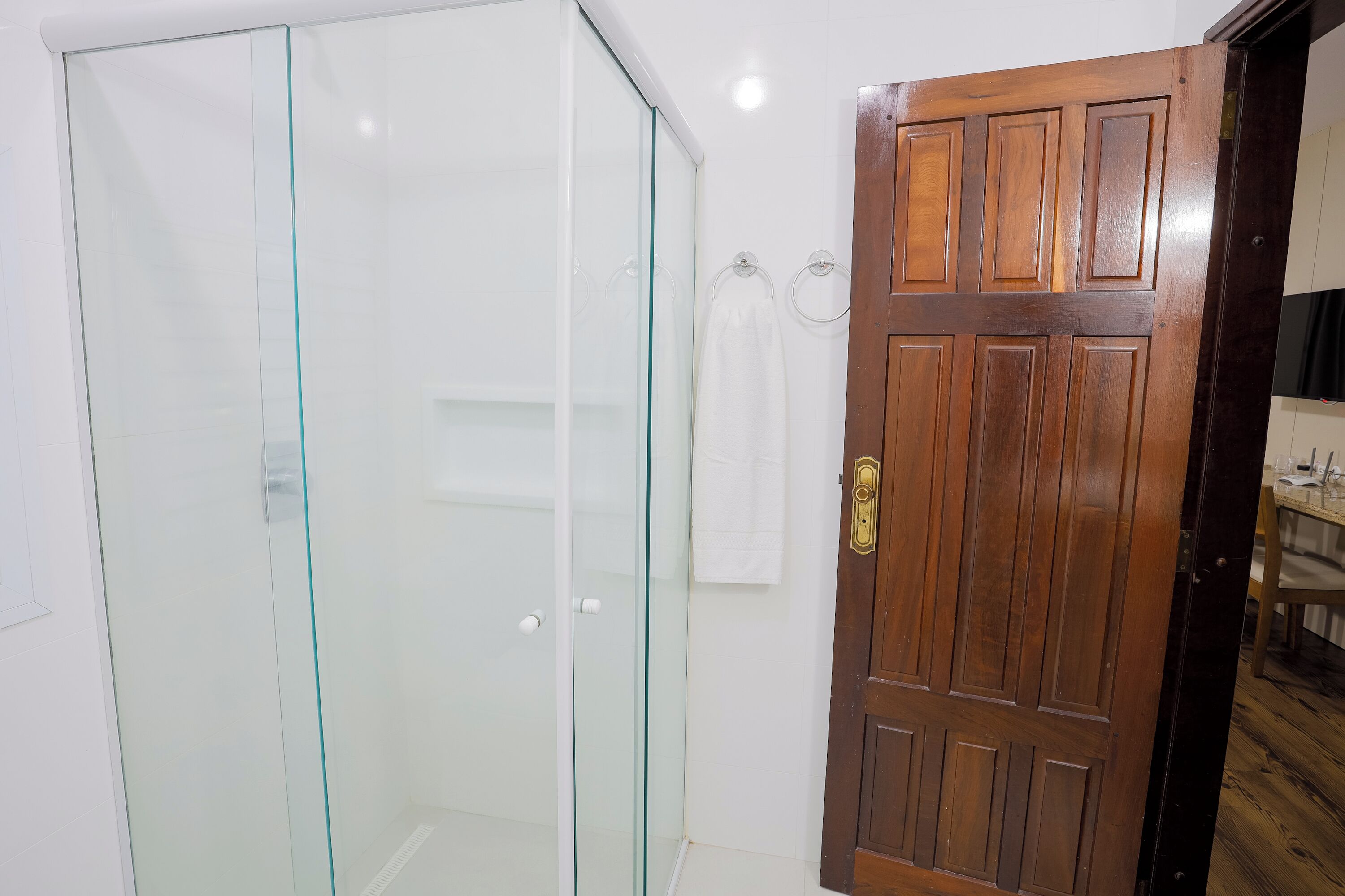 Un baño con cabina de ducha de vidrio, una puerta de madera y una toalla colgada en la pared.