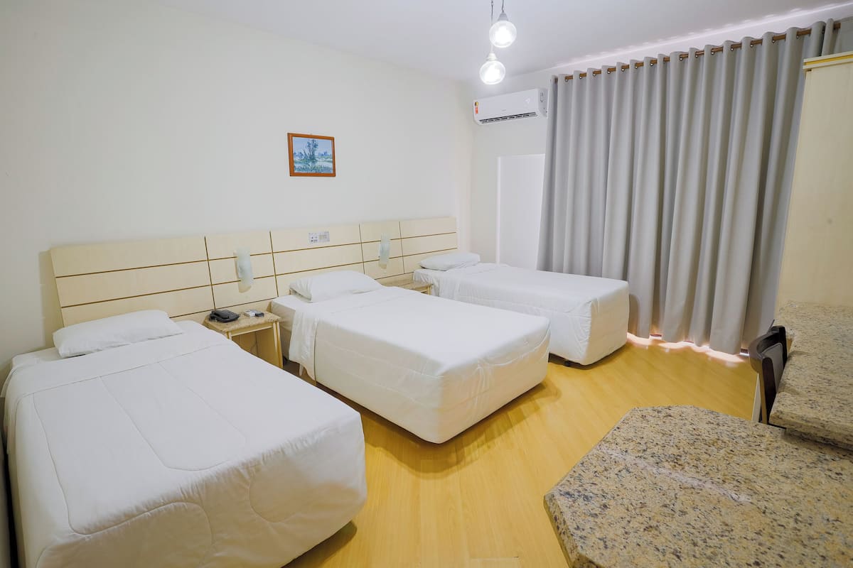 Hotellihuone, jossa on kaksi erillistä sänkyä, pieni pöytä, jossa on puhelin, tuoli ja ikkuna, jossa on verhot.