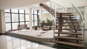 Un espacio interior amplio con una escalera moderna, ventanas grandes y un pequeño jardín con bancos y plantas.