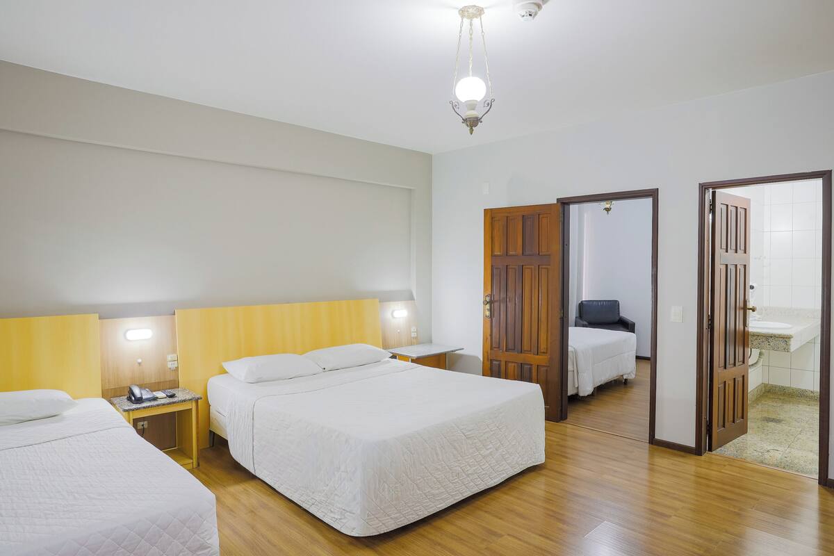 A hotel room with two beds, a desk, a chair, a mirror, and a bathroom visible through an open door.