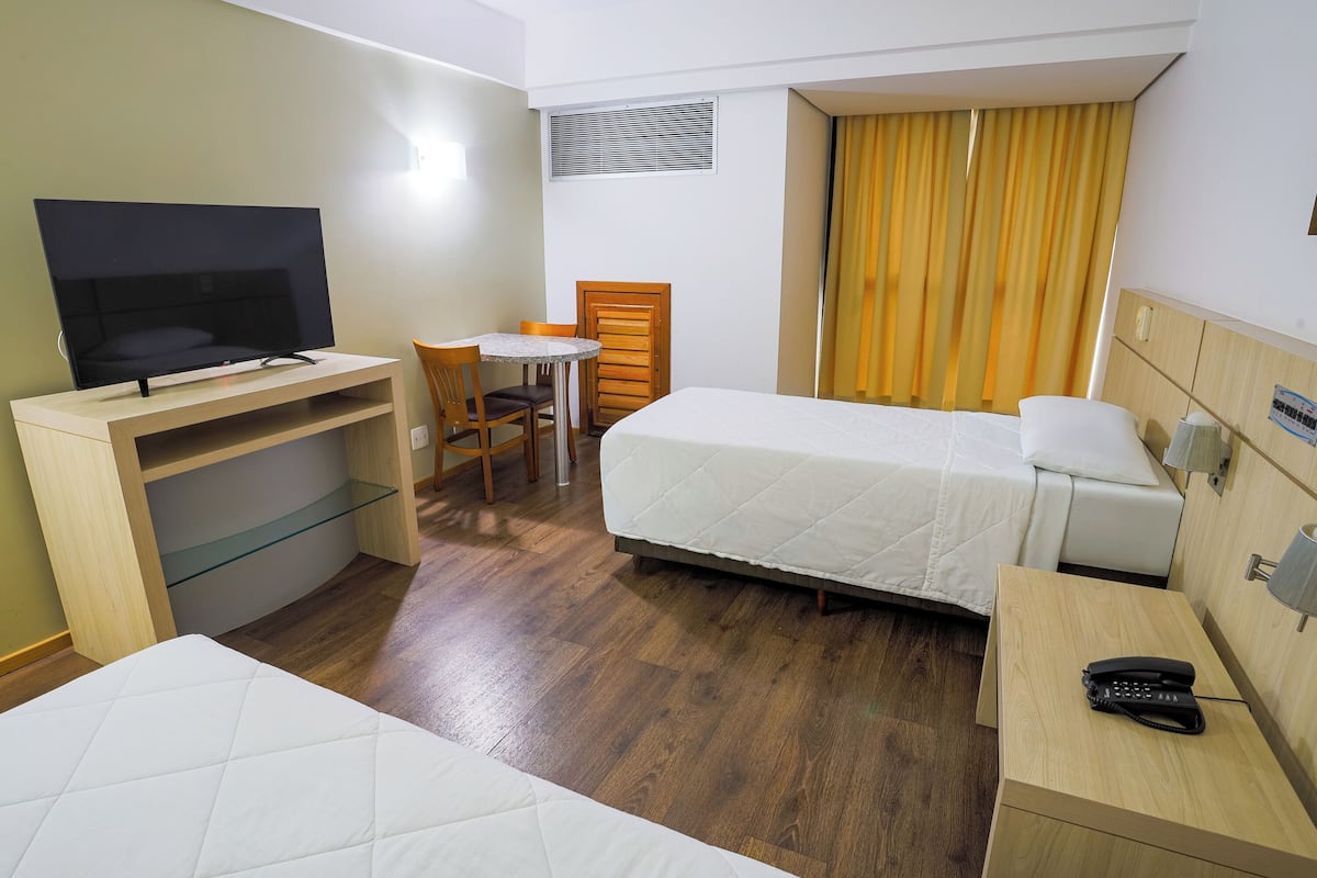 Hotellihuone, jossa on sänky, työpöytä, jossa on televisio, tuoli, pieni pöytä ja puhelin yöpöydällä.