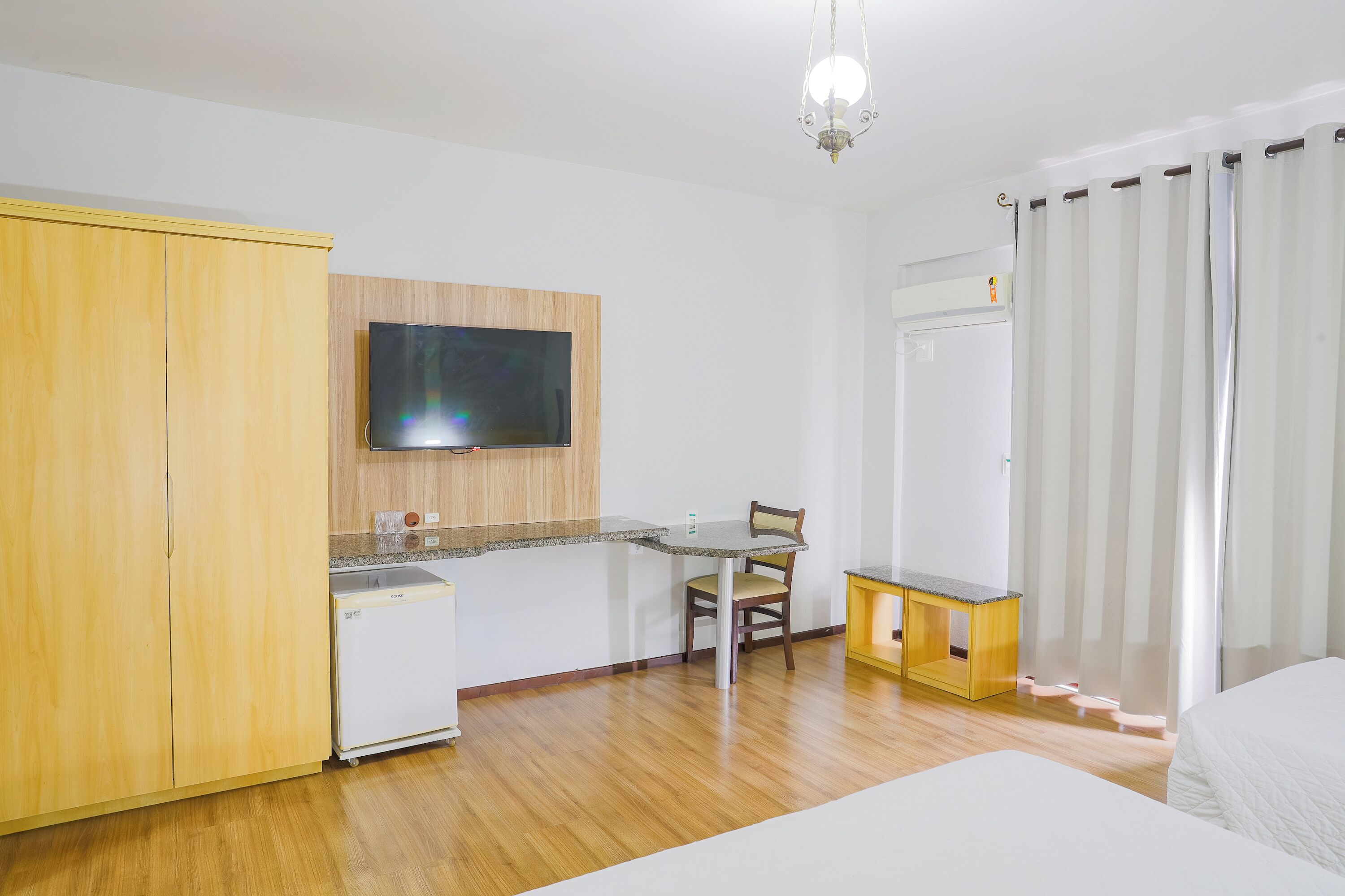 Una habitación de hotel compacta con kitchenette, cama, escritorio y silla.