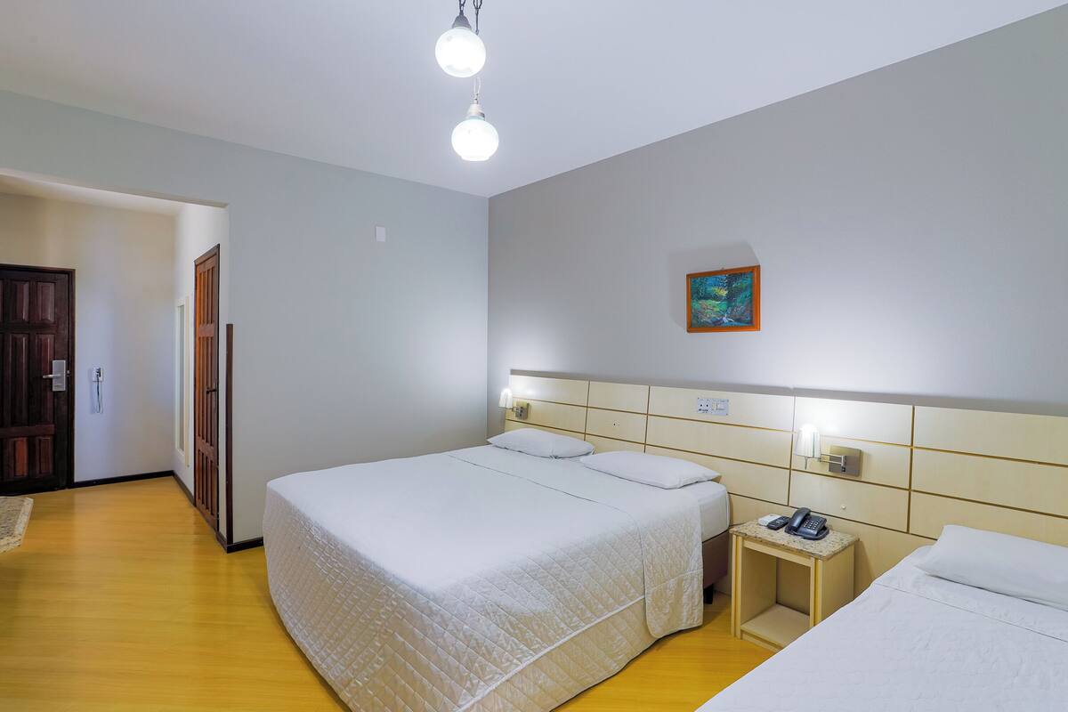 A hotel room with a large bed, bedside tables, a painting on the wall, and a door leading to another room.