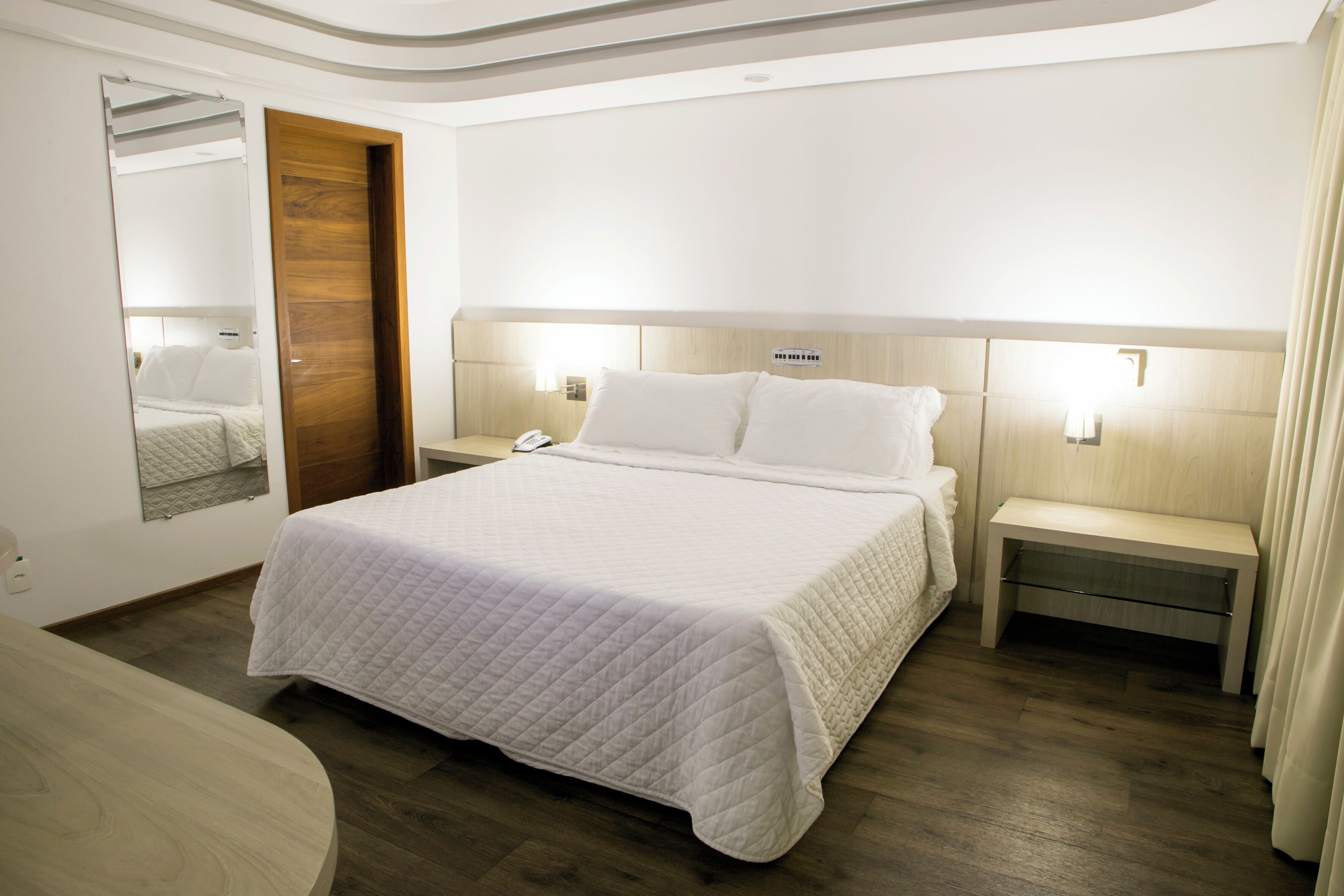 A hotel room with a large bed, bedside tables, a mirror, and a wooden door.