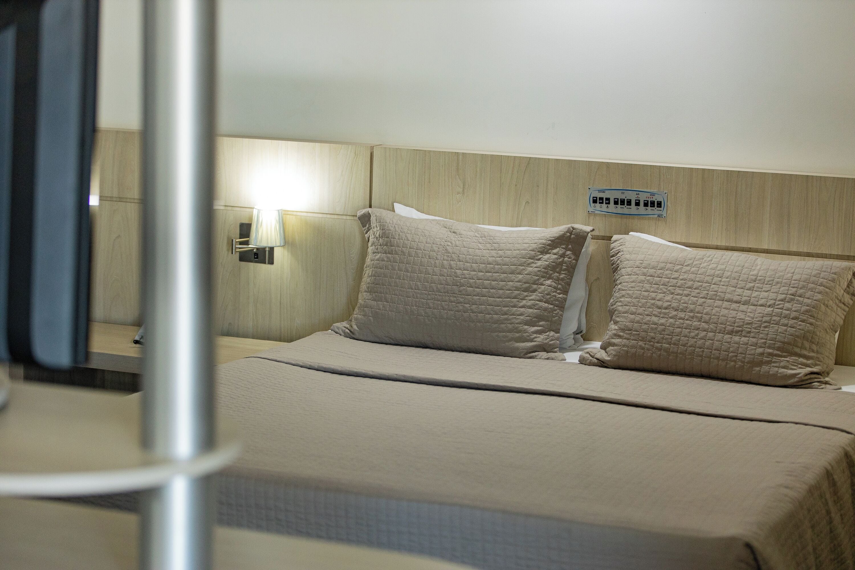 A hotel room with a bed, a nightstand, a lamp, and a wall socket.