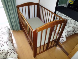 Un berceau en bois avec un matelas, placé dans une pièce où se trouvent une couvre-lit à motifs et un rideau vert.
