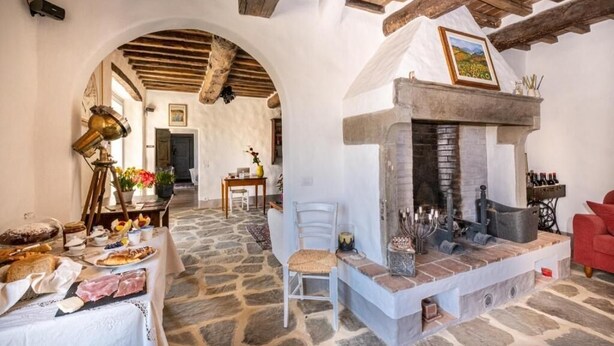 A rustic interior with a stone floor, a fireplace, and a dining area with food and drinks. - Podere Fontanino (Arezzo)