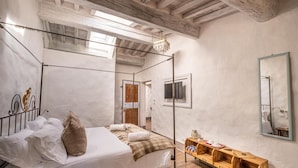 A four-poster bed with a wooden headboard, a wooden nightstand with a lamp, and a large mirror on the wall. - Podere Fontanino (Arezzo)