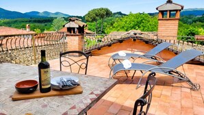 Una terraza con mesa lista para comer, una botella de vino y sillones de descanso.