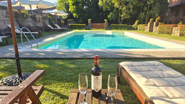 Escena junto a la piscina con una botella de vino, dos copas y un banco acolchado.
