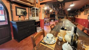 Un restaurante acogedor con una larga mesa de madera, botellas de vino y una chimenea.