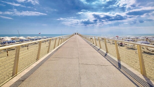 Un paseo marítimo con un camino de hormigón, sombrillas de playa y una vista despejada del océano.