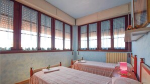 Una habitación con dos camas, ventanas amplias con persianas, un radiador y un espejo.