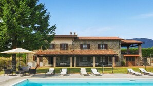 Un bâtiment en pierre doté d’une piscine, de chaises longues et d’un patio couvert.