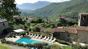 A pool area with lounge chairs, a stone building with a bell tower, and a mountainous landscape in the background. - Costola, private pool, stunning mountain views. Chef on request. (Fosciandora)