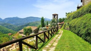 A stone pathway leading to a rustic stone building with a bell tower, surrounded by lush greenery and mountains in the background. - Costola, private pool, stunning mountain views. Chef on request. (Fosciandora)