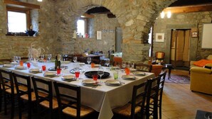 A stone-walled dining area with a long table set for a meal, wooden chairs, and a cozy living area with a sofa and a television. - Costola, private pool, stunning mountain views. Chef on request. (Fosciandora)