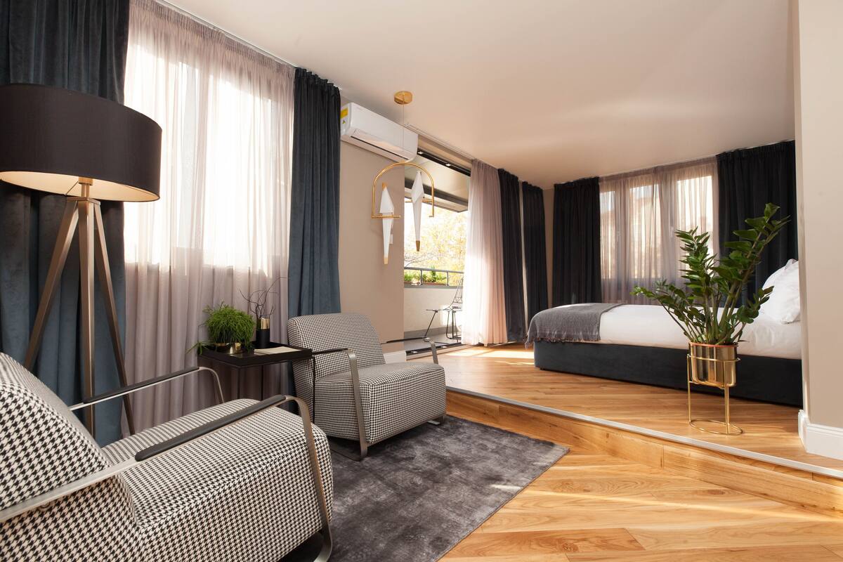 A modern bedroom with a bed, a sofa, a chair, a small table, and a potted plant.