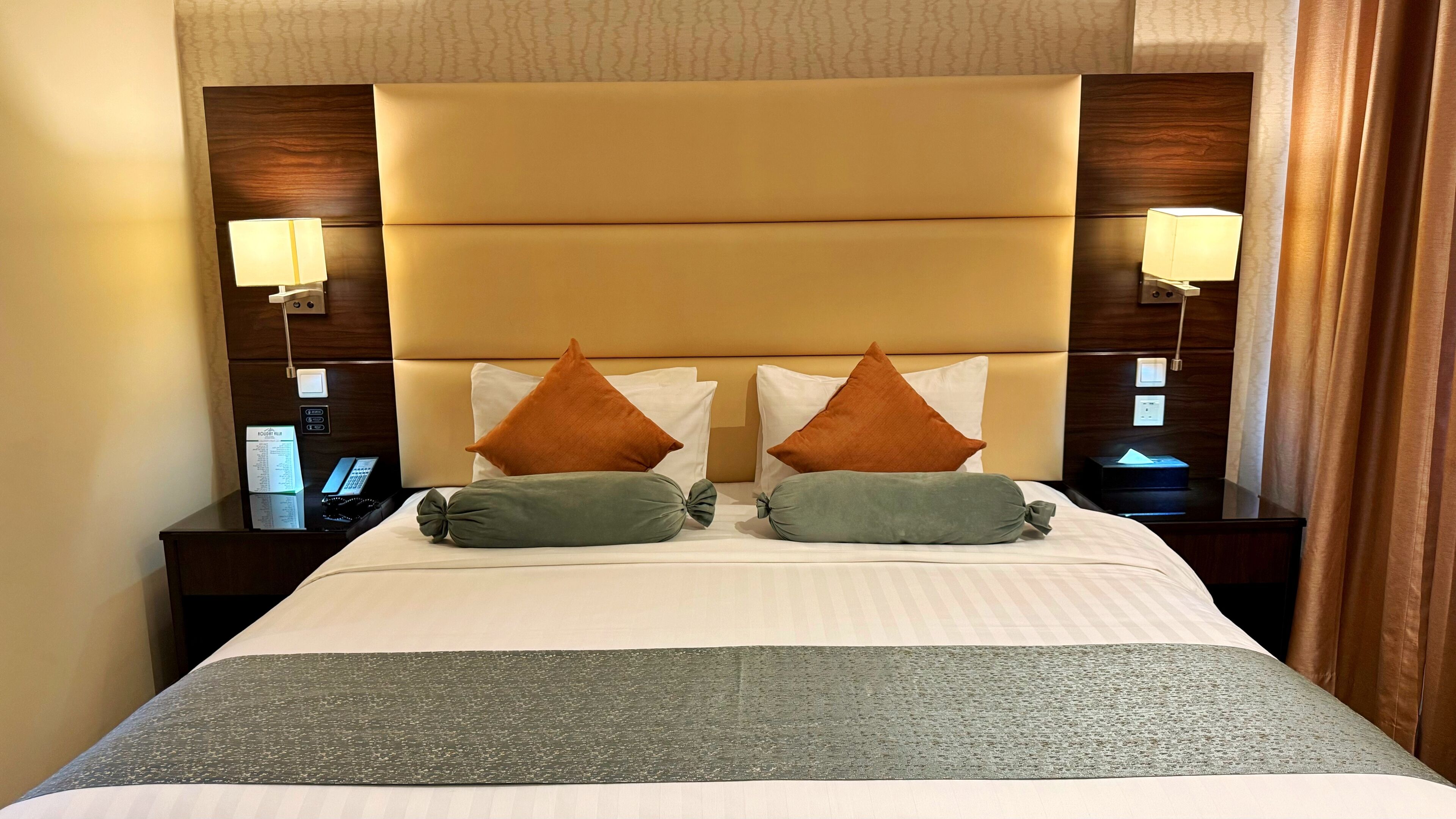 A hotel room with a large bed, two nightstands, a headboard, and two wall-mounted lamps.