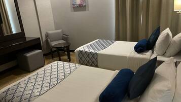 Ein Hotelzimmer mit zwei Betten, einem Sessel, einem Schreibtisch und einem Spiegel.