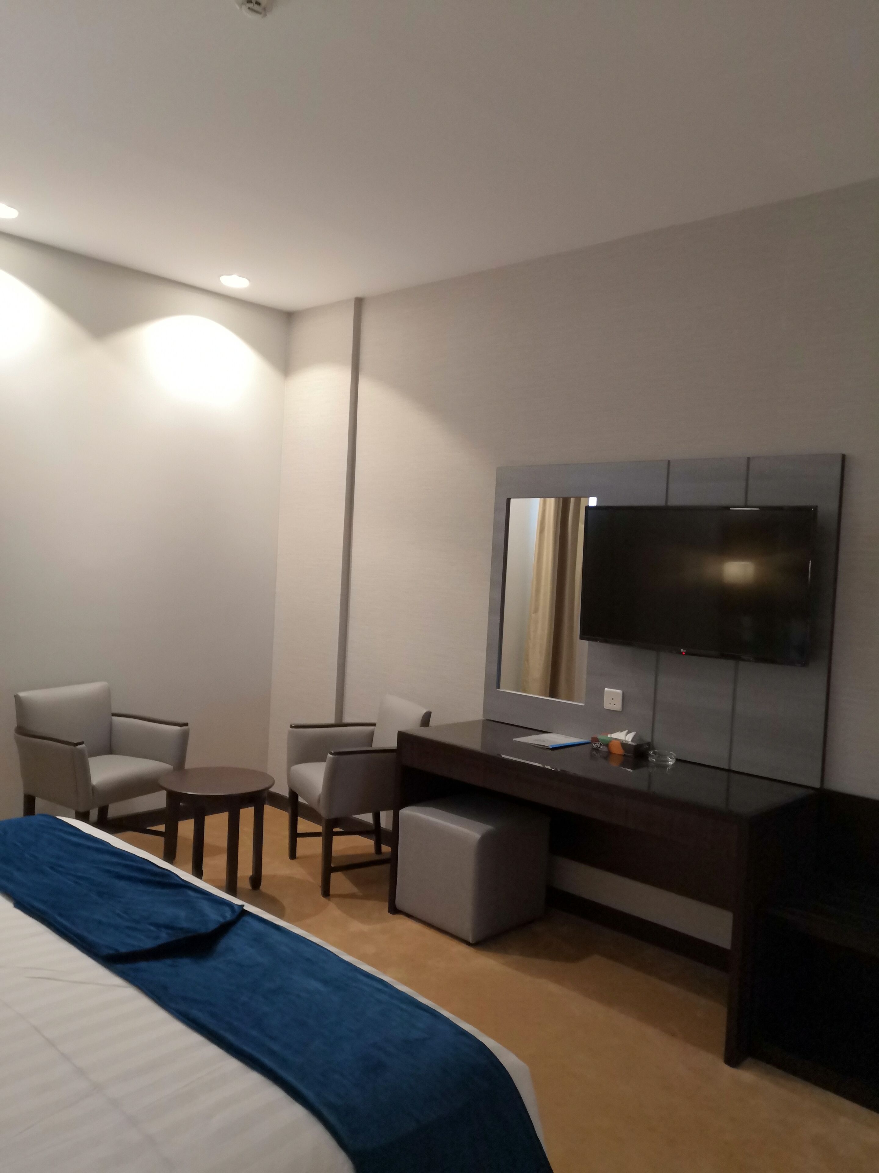A hotel room with a bed, a desk, a chair, a TV, and a small table.