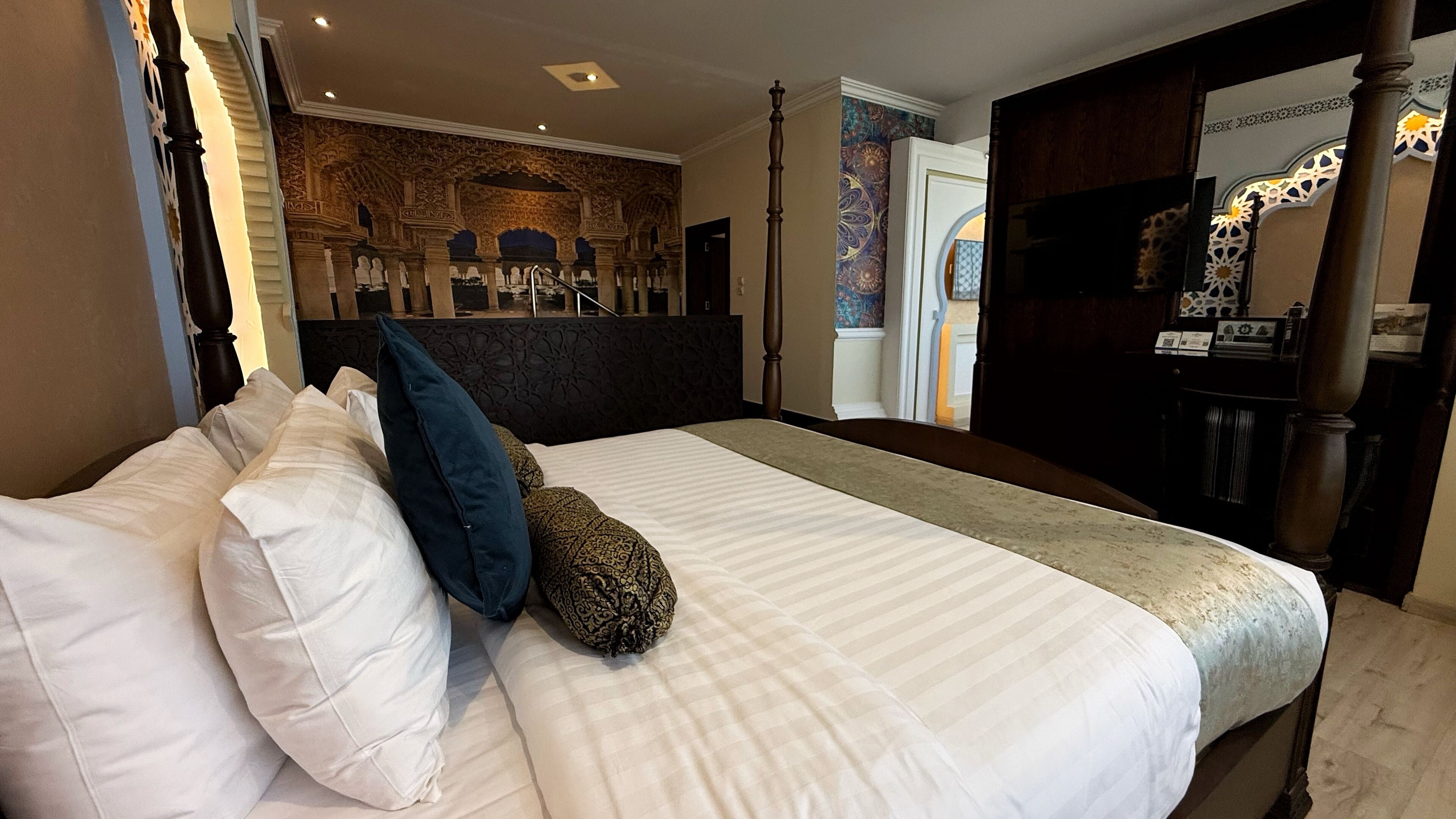 A hotel room with a large bed, a dark headboard, and a decorative wall with intricate patterns.