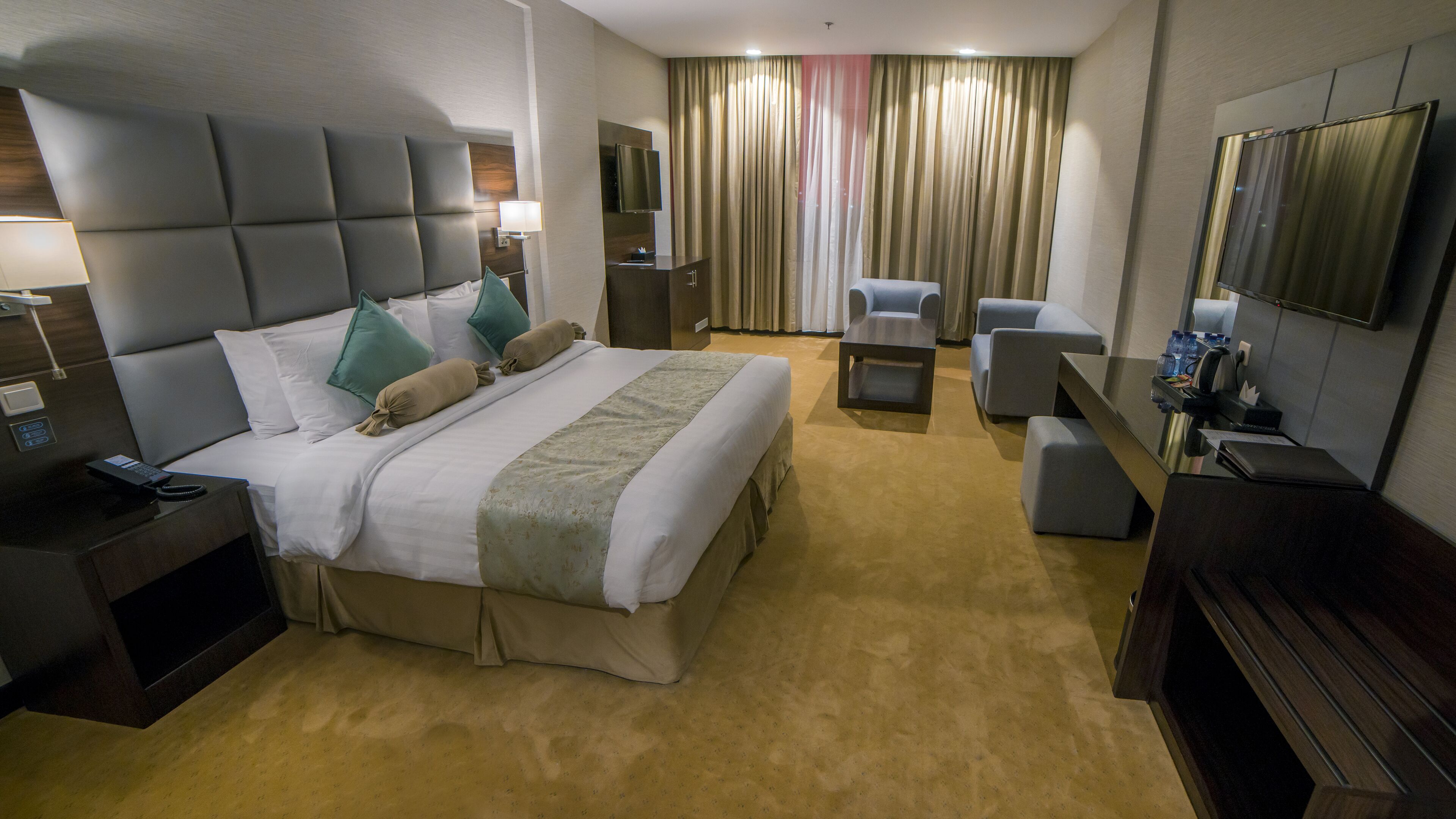 A hotel room with a large bed, a desk, a chair, a TV, and a window with curtains.