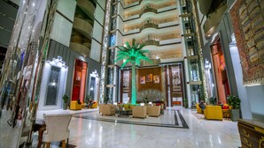 A spacious lobby with a central palm tree, multiple seating areas, and a high ceiling with balconies. - Holiday Villa Hail Hotel (Ha'il)
