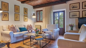 A living room with a sofa, armchairs, a coffee table, and a TV. There are framed pictures on the walls and a window with curtains. - Home Cinema • Private Pool & Hot Tub • Sleeps 12 (6 Bathrooms) (Pergine)