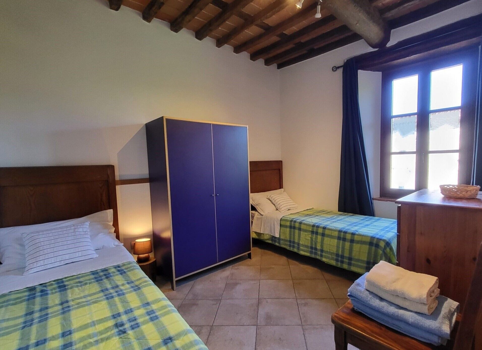 Une chambre avec deux lits, une armoire, une fenêtre avec des rideaux et une petite table avec des serviettes.