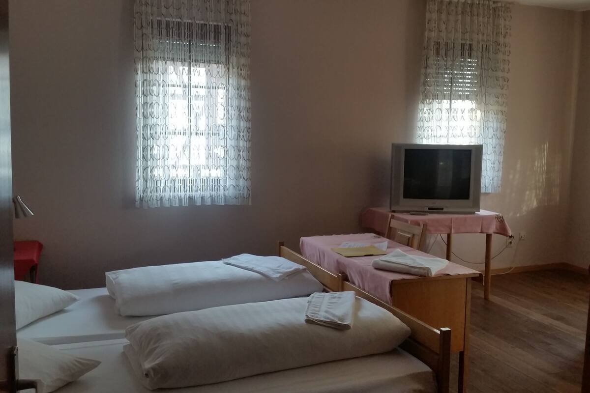 A hotel room with two beds, a television on a small table, and curtains on the windows.