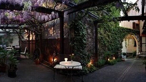 An indoor dining area with tables and chairs, a fire pit, and a pergola with purple flowers. - Adler Gaststube Hotel Biergarten (Bad Rappenau)
