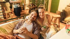 A couple sitting on a bed in a room with a table and chairs, a green door, and a Christmas tree in the background. - Arena Nest Hostel (Santiago del Teide)
